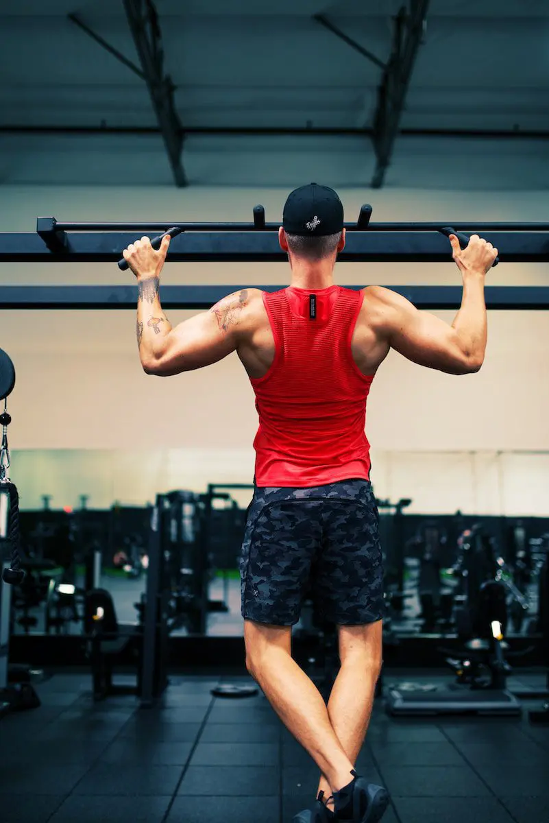 man in red tank top and black shorts holding black dumbbell